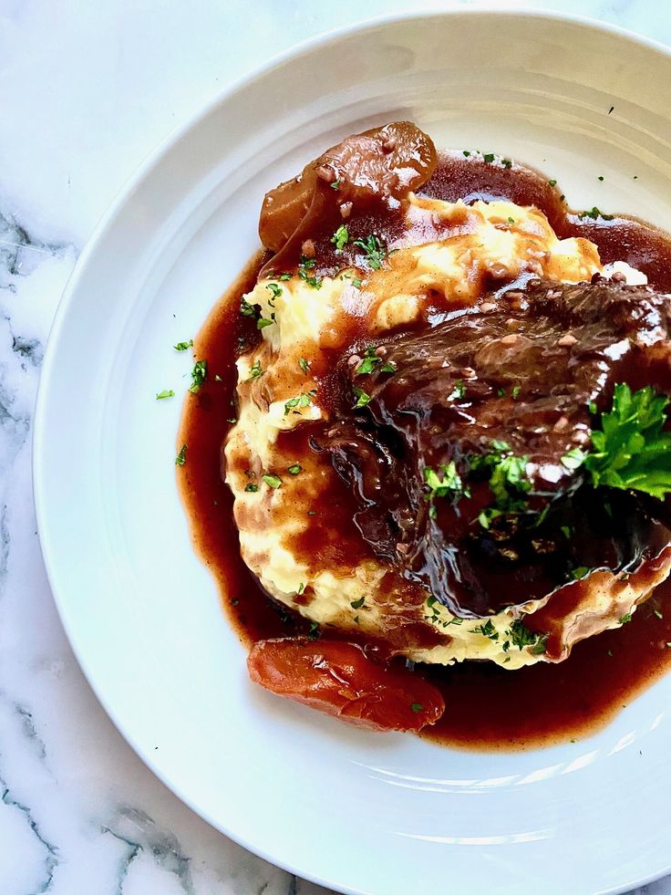 a white plate topped with meat and gravy on top of a marble table