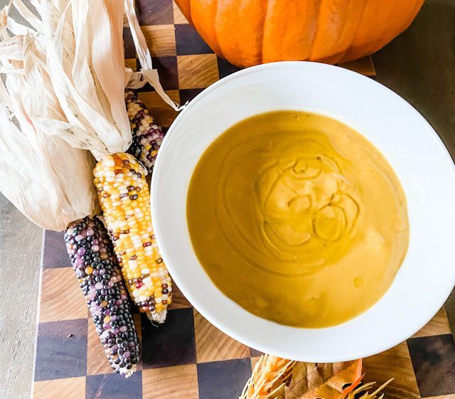 a white bowl filled with soup next to corn on the cob and pumpkins