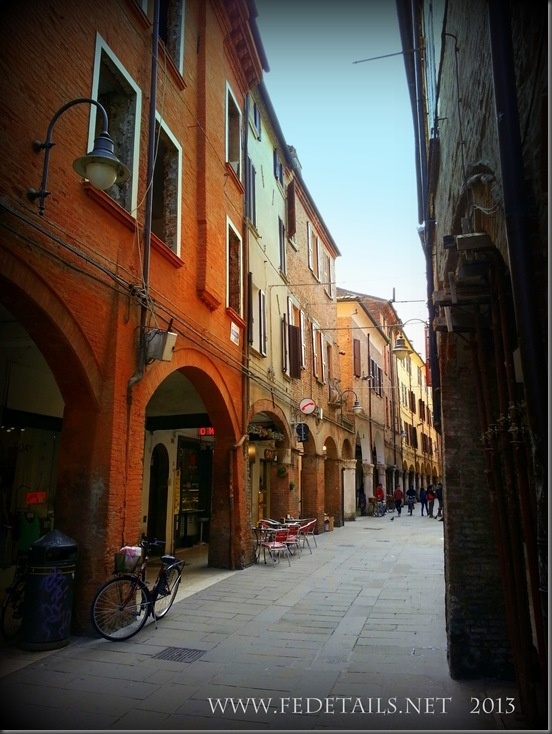 an alley way with tables and chairs on both sides, surrounded by tall brick buildings