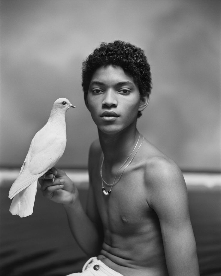 a man holding a white bird in his right hand and wearing a necklace on it's neck