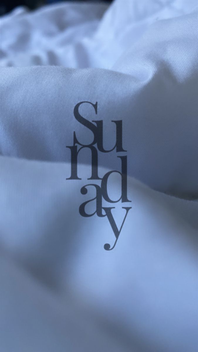 the word surdday is written in black on a white bed sheet with an unmade pillow