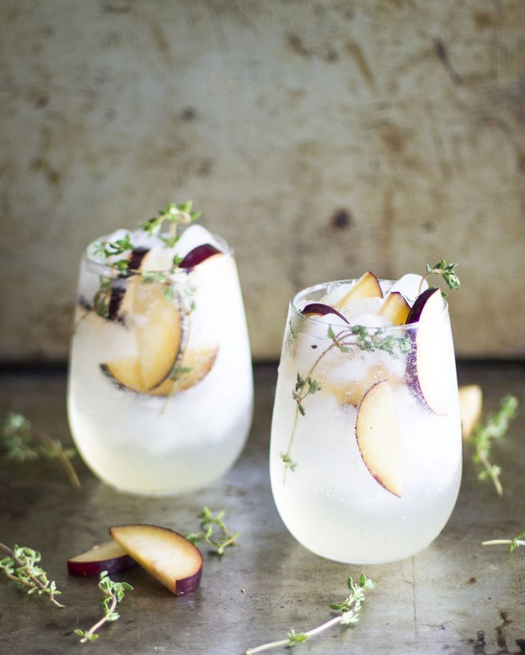 two glasses filled with ice and fruit on top of a table