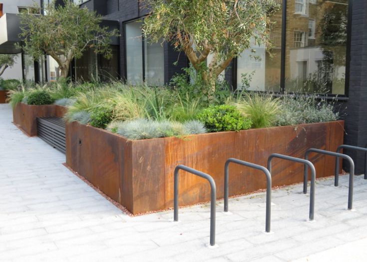 a large metal planter filled with lots of plants next to a tall black building