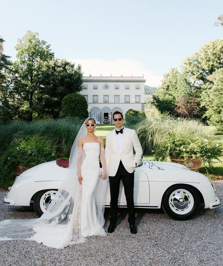 a bride and groom standing in front of a classic car