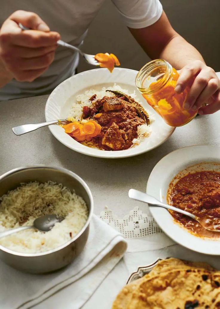 a person sitting at a table with plates and bowls of food in front of them