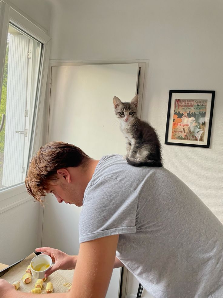 a cat sitting on the back of a man's shoulders as he looks at something