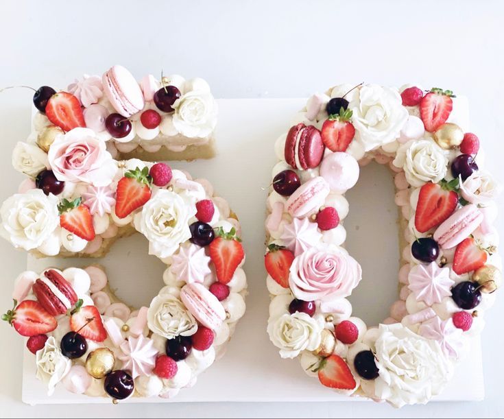 there is a cake shaped like the number 50 made out of fruit and flowers on a white surface