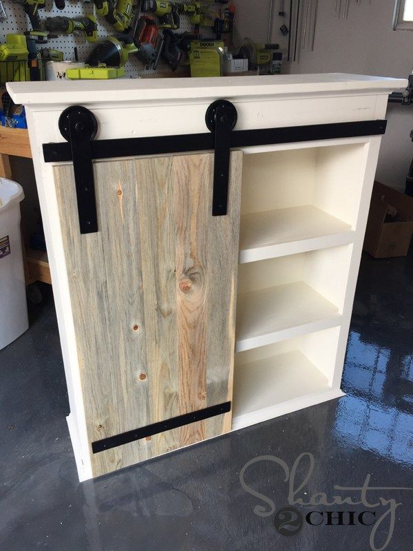 an unfinished cabinet with black straps on the door and shelves in the back, inside a garage