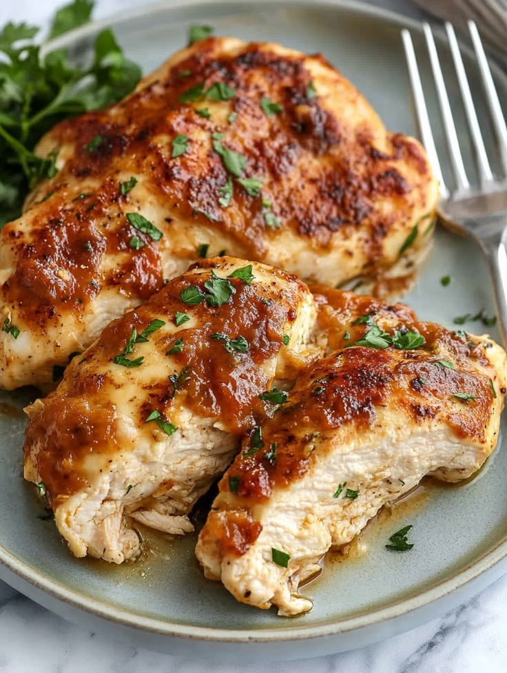 two pieces of chicken covered in marinara sauce and parsley on a plate with a fork