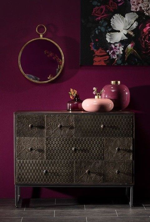 an ornate dresser with pink vases and paintings on the wall in front of it