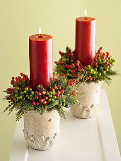 two red candles sitting on top of a white table with greenery and berries in them