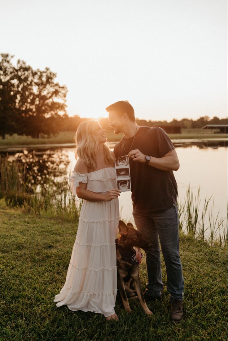 a man and woman standing in front of a lake with a dog next to them