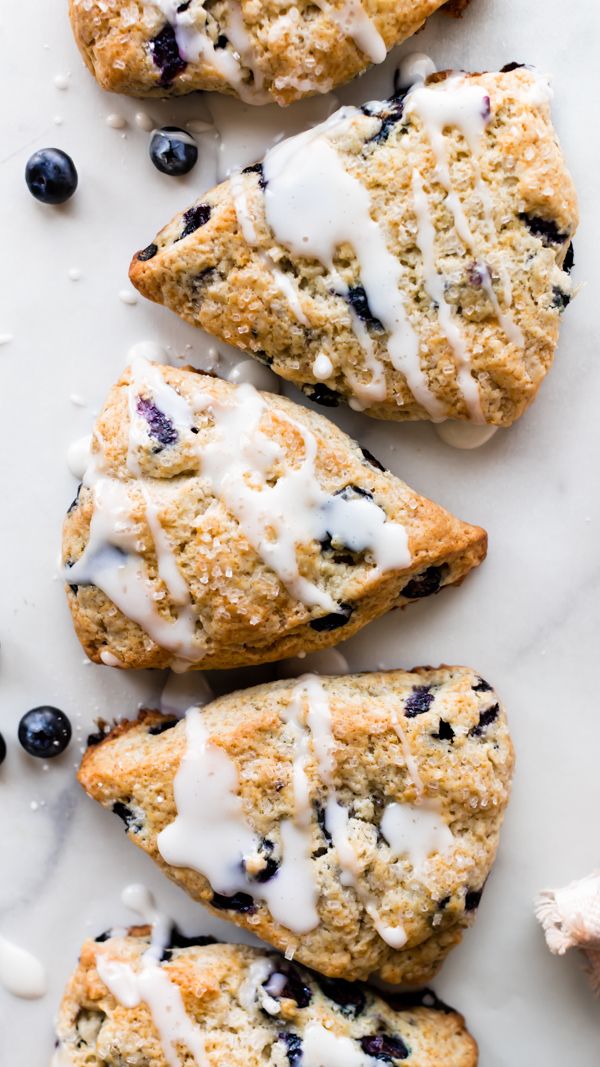 blueberry scones with white icing and fresh blueberries scattered around them on a marble surface