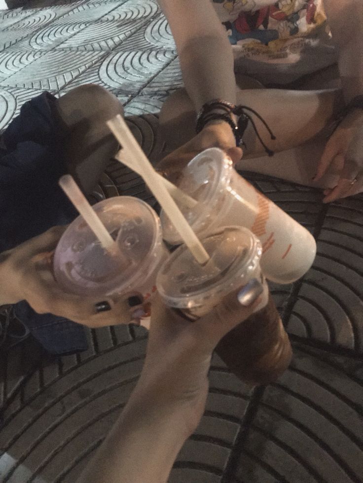 two people holding up cups with straws in them