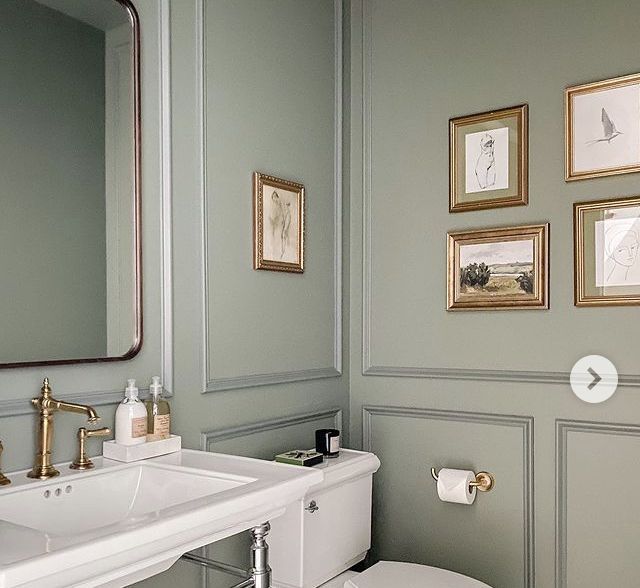 a white toilet sitting next to a sink in a bathroom under framed pictures on the wall