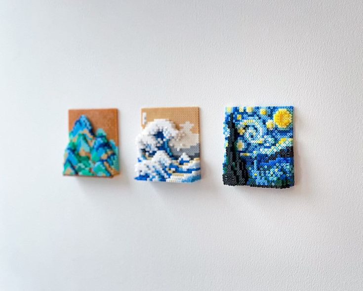 three small pieces of beaded art hanging on a white wall next to each other