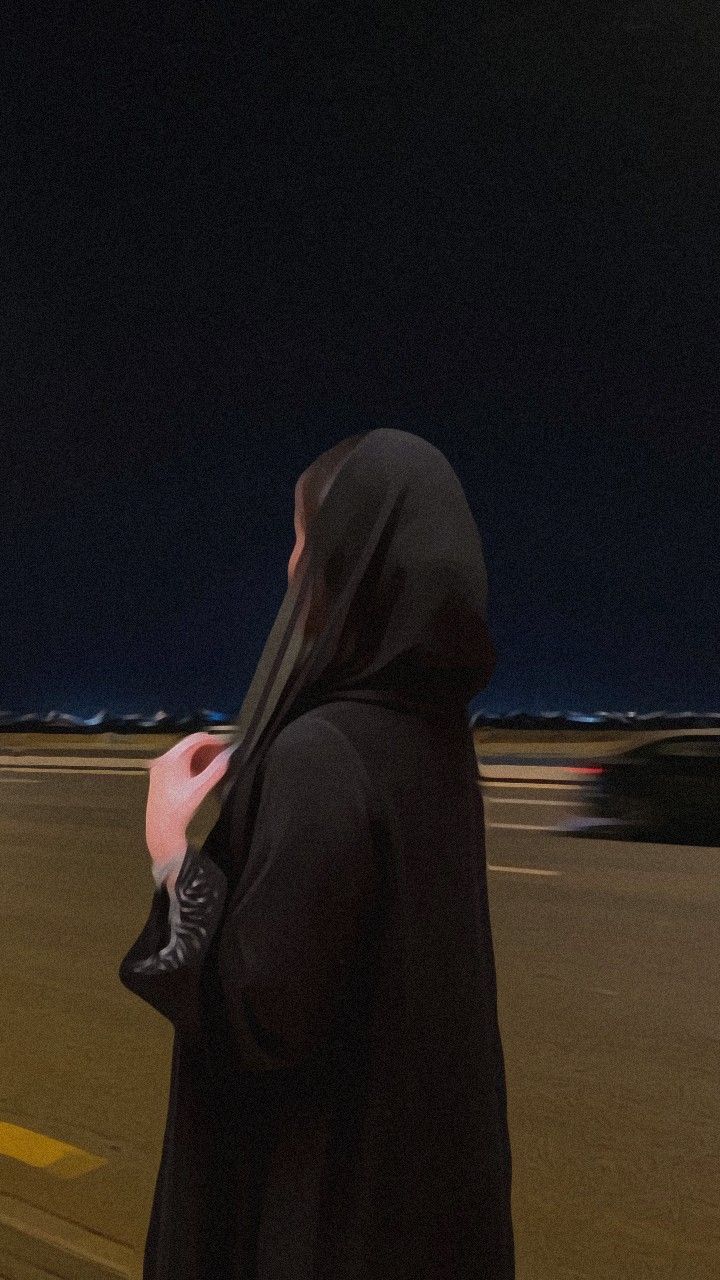 a woman walking down the street at night wearing a black hoodie and carrying a purse