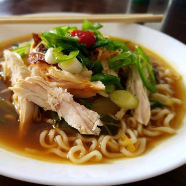 a white plate topped with noodles and meat next to chopsticks on a table