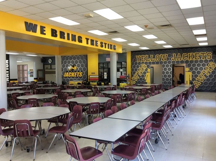 an empty cafeteria with tables and chairs in the center, yellow lettering on the wall