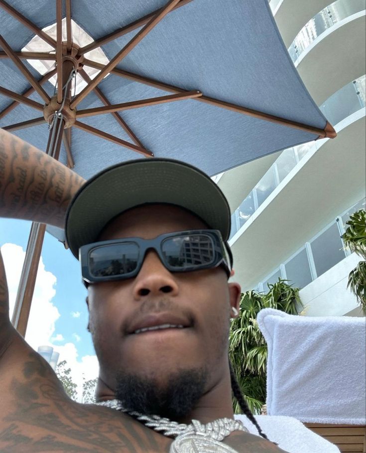 a man wearing sunglasses and a hat with tattoos on his arm is holding an umbrella over his head