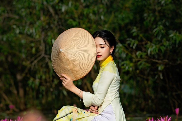 a woman sitting on the ground with a large umbrella over her head in front of trees