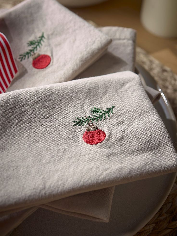 three white towels with embroidered designs on them sitting on a plate next to a red and white striped napkin