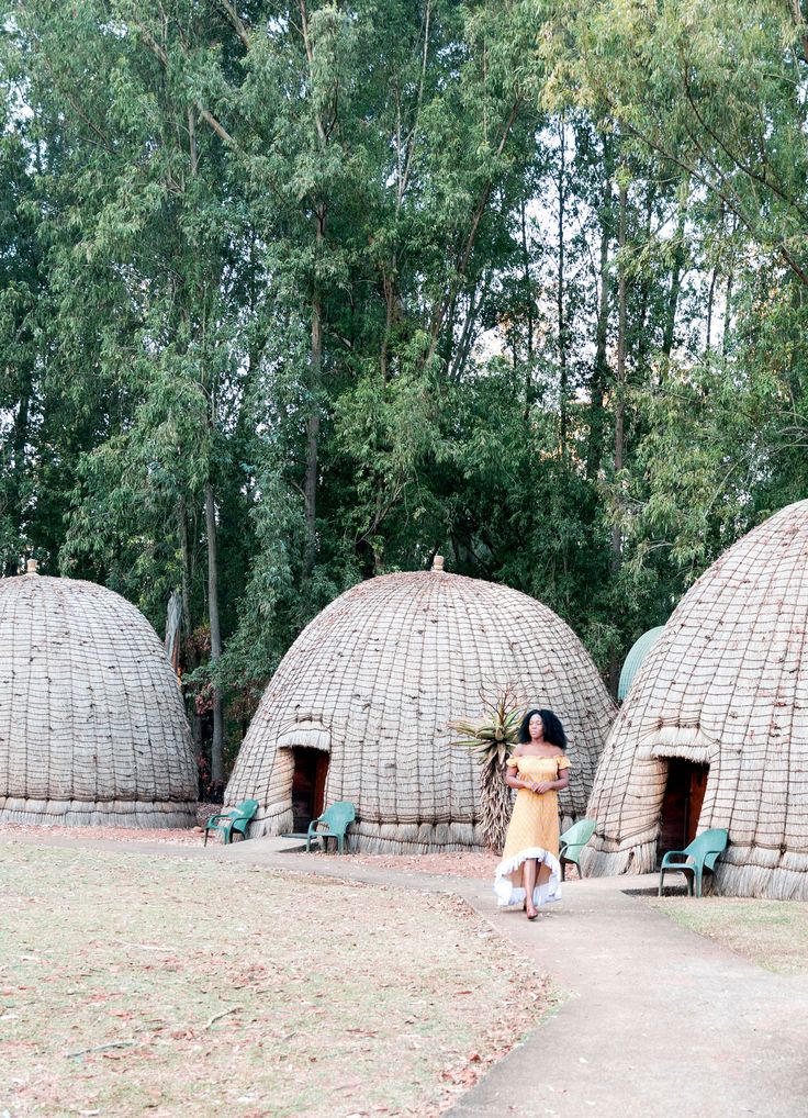 a woman is standing in front of some huts that are made out of sticks and grass