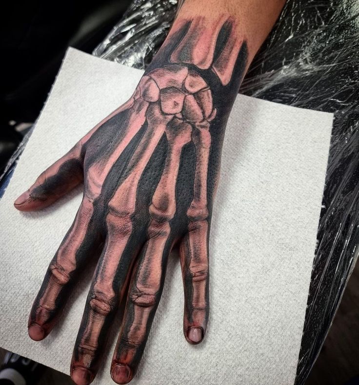 a person's hand with a black and grey skeleton design on it, sitting on top of a piece of paper