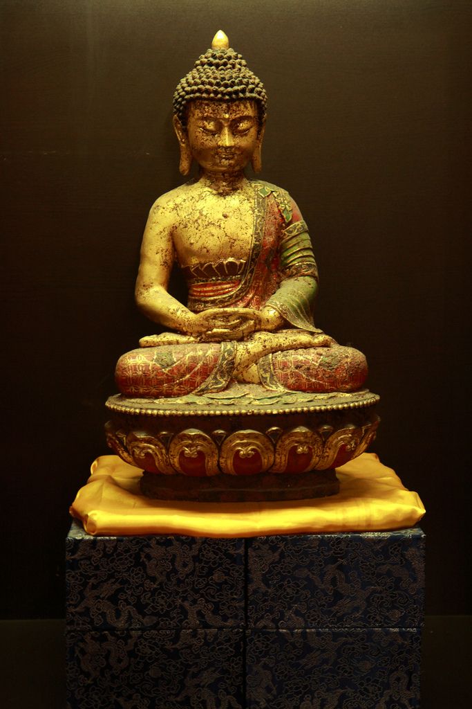 a golden buddha statue sitting on top of a wooden block in front of a black wall