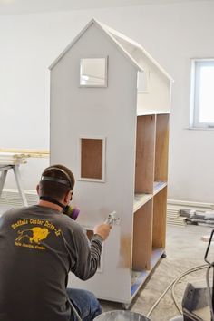 a man is painting the side of a small white house with wood trimmings