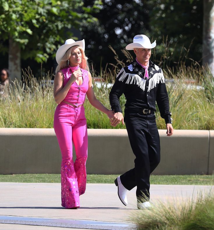 a man in a cowboy hat and pink outfit walking next to a woman in a pink jumpsuit