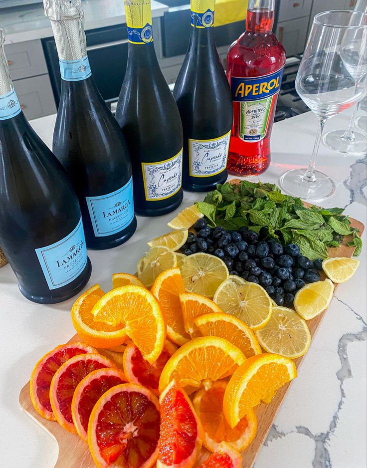 several bottles of wine and orange slices on a cutting board with blueberries, raspberries, lemons, and spinach