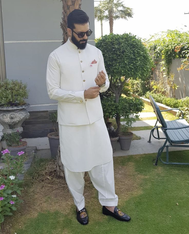 a man standing in the grass wearing a white suit and black shoes with his hand on his hip