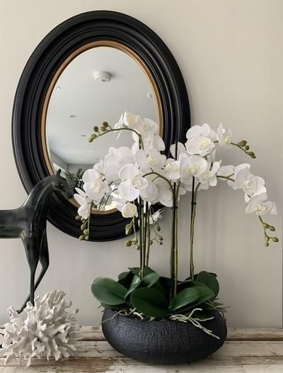 white flowers in a black vase on a table next to a mirror and horse figurine