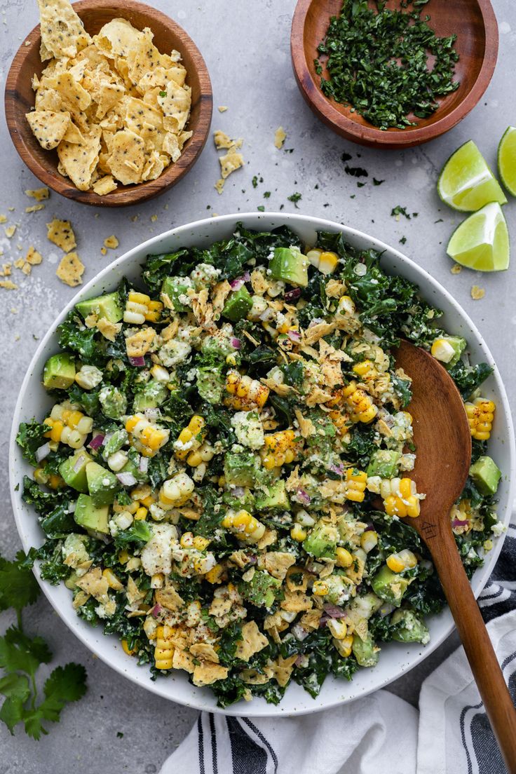 a bowl filled with corn and vegetables next to two wooden spoons on top of a table