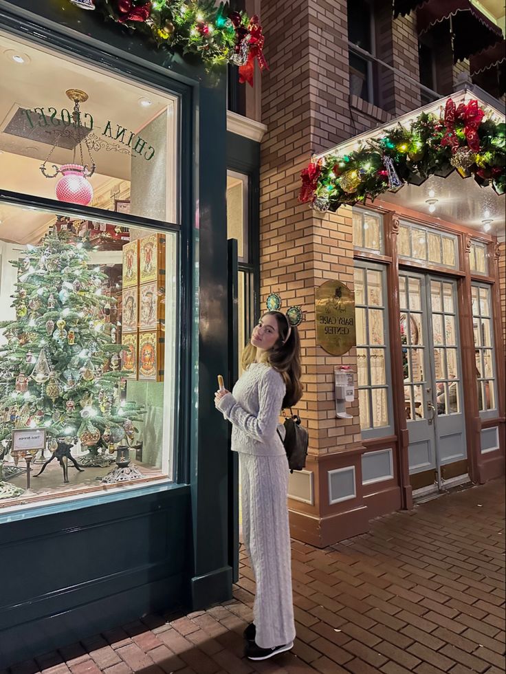 a woman standing in front of a store window with christmas decorations on the windowsill