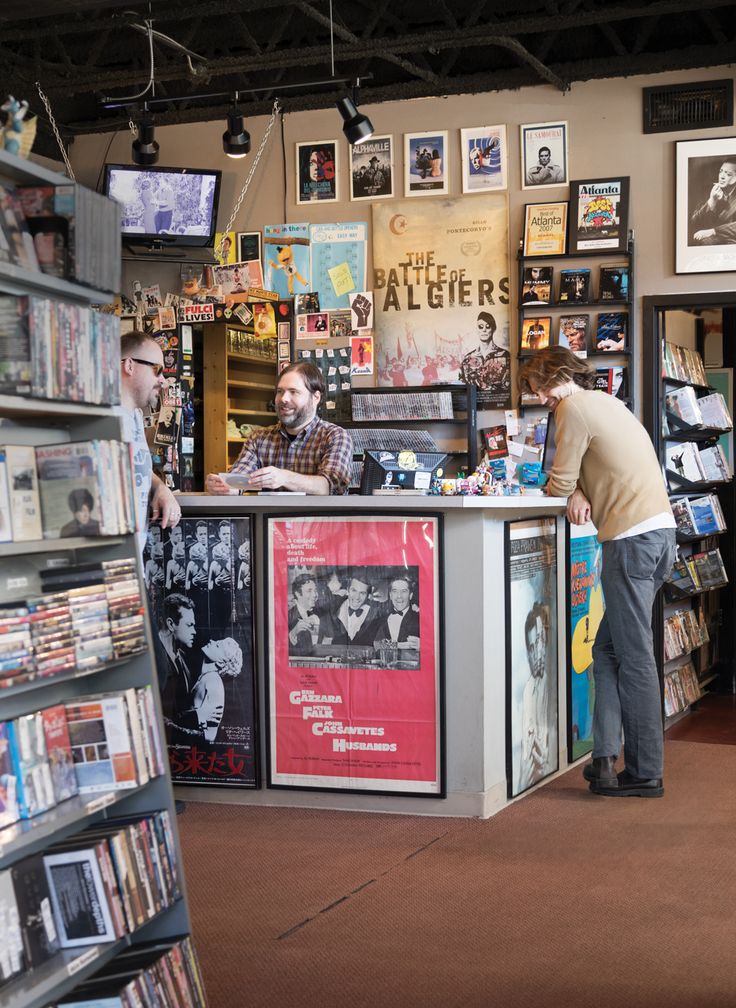 two men standing in front of a book store with books on the shelves and posters on the walls