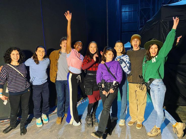 a group of people standing next to each other in front of a black wall with their arms up