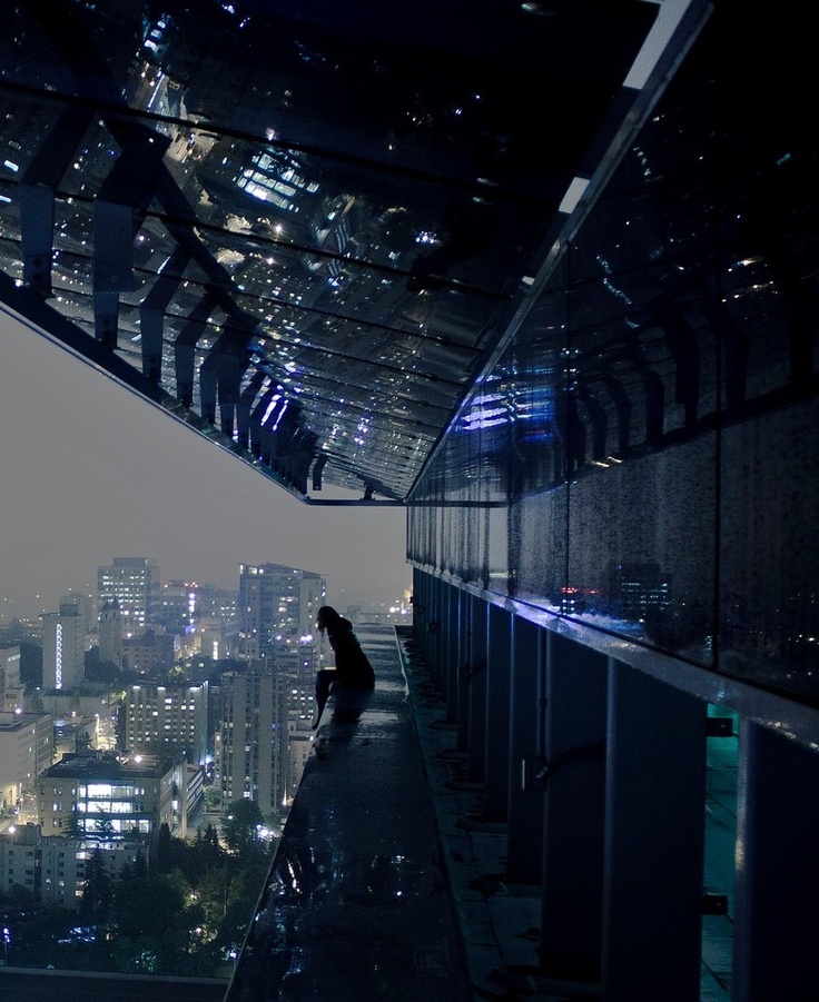 a person standing on the edge of a building at night with city lights in the background