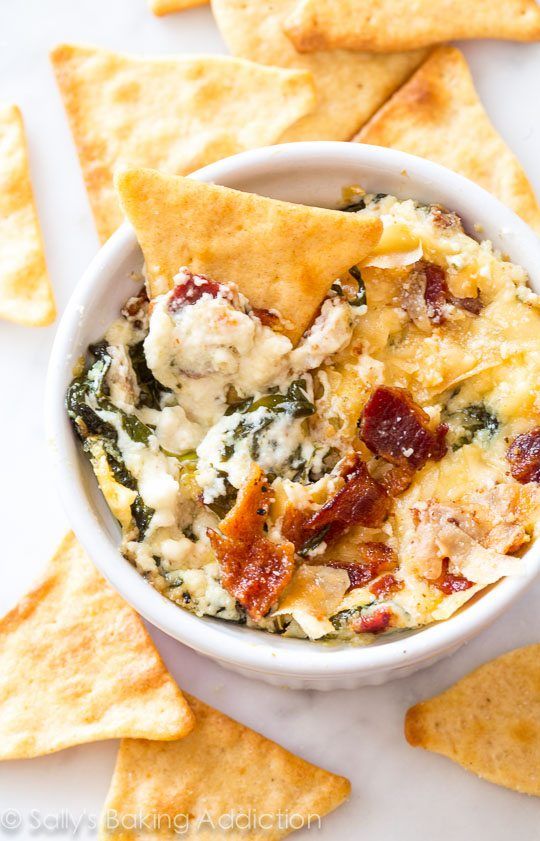 spinach dip with bacon and cheese in a white bowl surrounded by tortilla chips