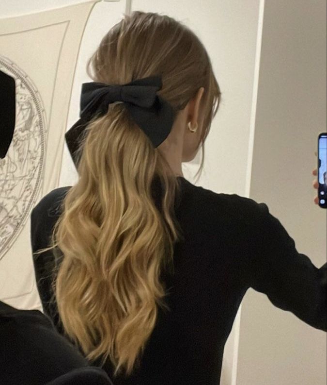 a woman with long blonde hair wearing a black bow in her hair and looking into the mirror