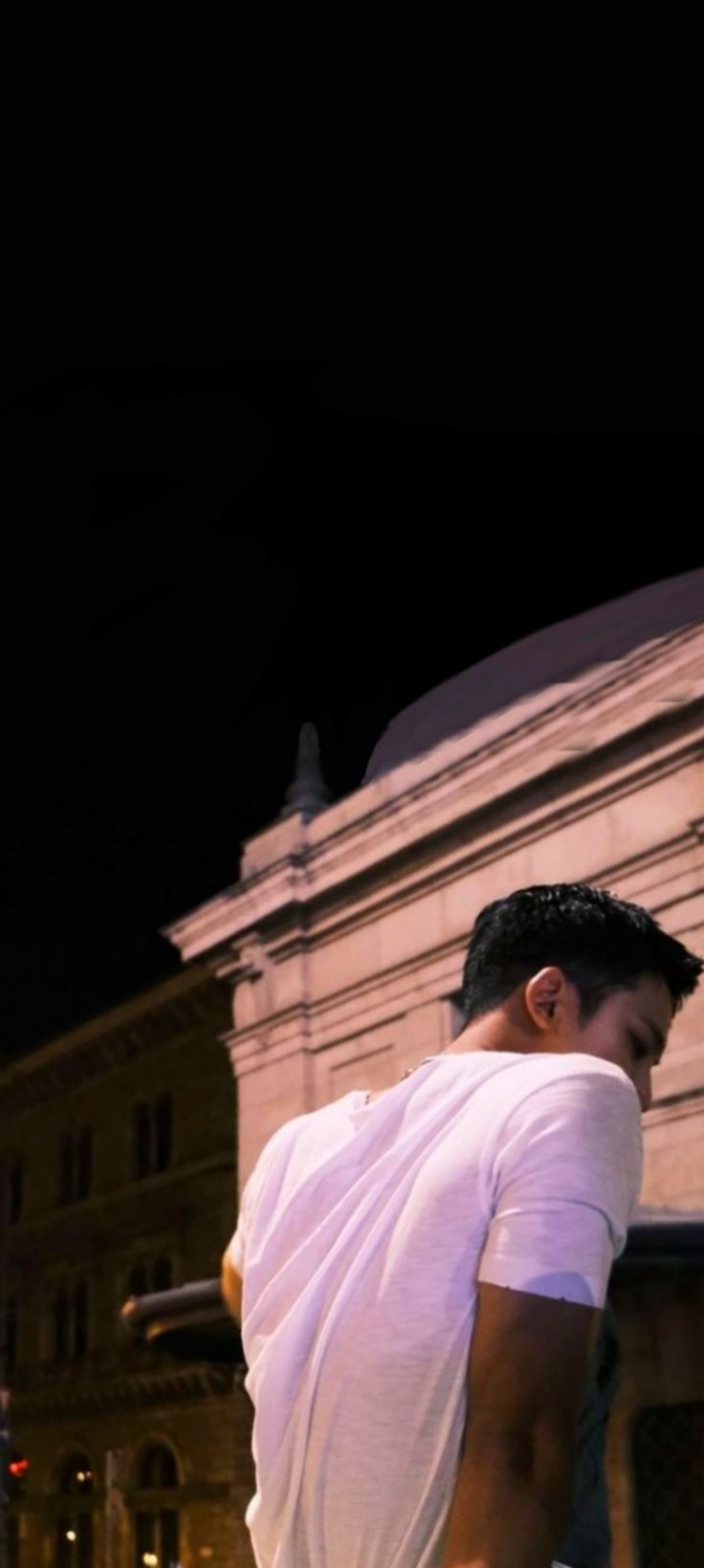 a man riding a skateboard down the side of a road at night with buildings in the background