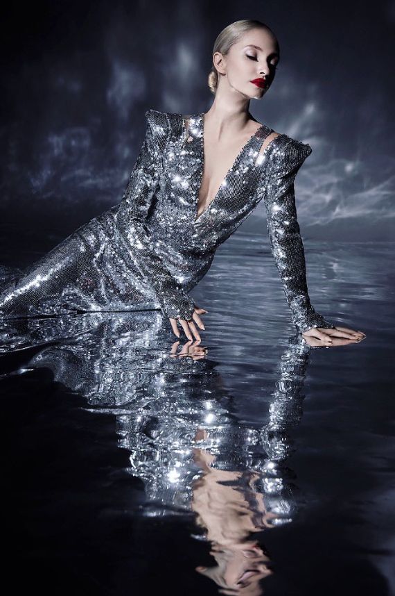 a woman is sitting in the water with her legs spread out and wearing silver sequins