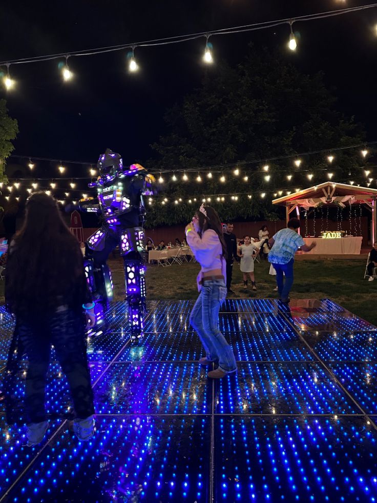 some people are standing around with blue lights on the ground and one person is holding a cell phone