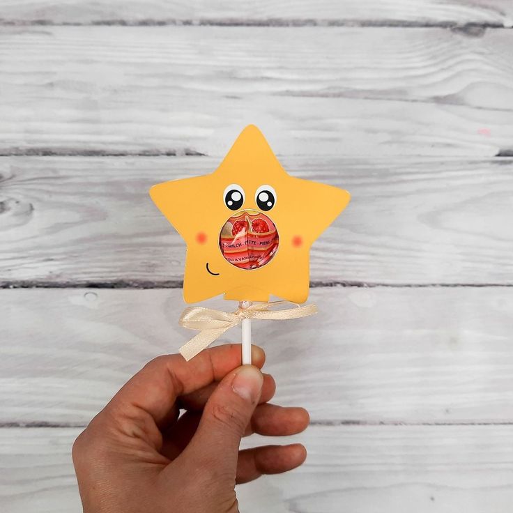 a hand holding up a yellow star shaped lollipop on a white wooden background