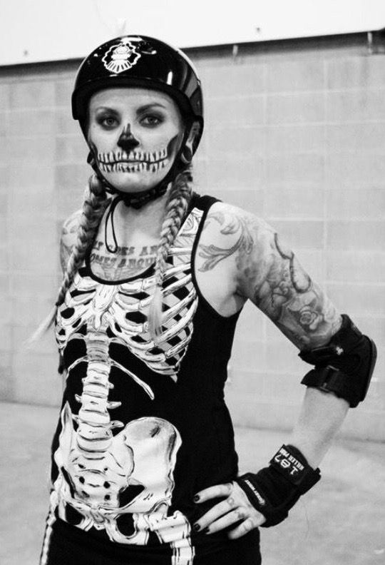 a woman wearing a skeleton costume and helmet with her hands on her hips while standing in front of a brick wall