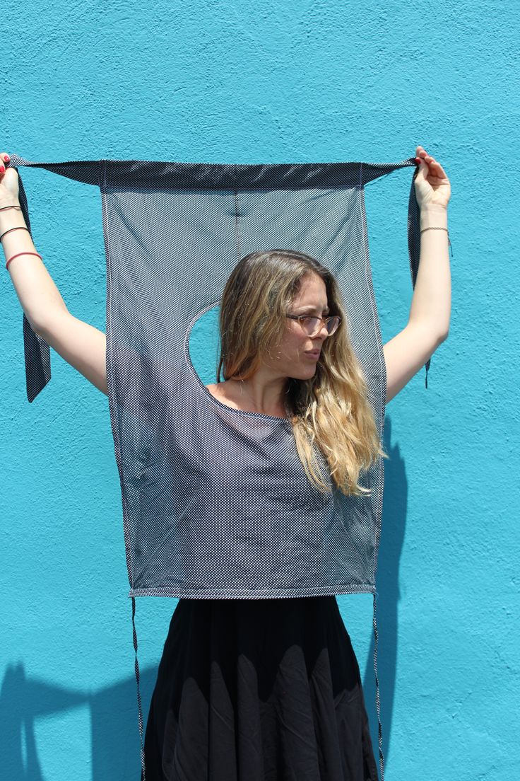 a woman standing in front of a blue wall holding up a black piece of cloth