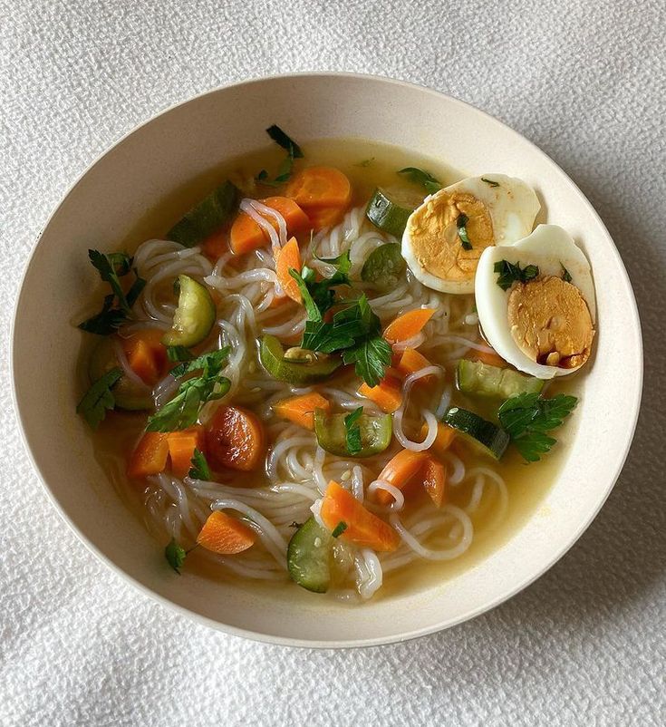 a white bowl filled with noodles, carrots and hard boiled egg on top of a towel