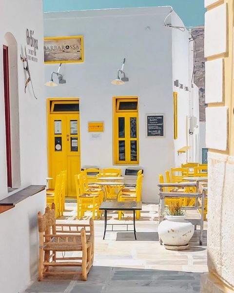 an alley way with yellow chairs and tables on the sidewalk in front of white buildings