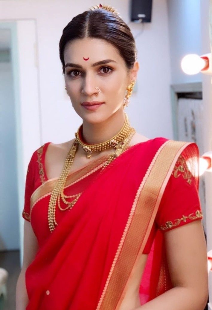 a woman in a red sari with gold jewelry on her neck and chest is posing for the camera